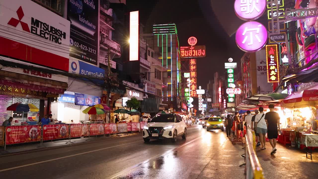 Pedestrians walk past colorful neon-lit street food stalls in bustling Chinatown, Bangkok at night
