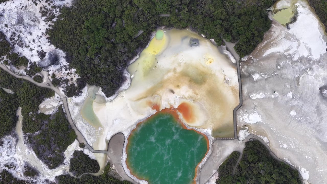 Letecký pohled na barevný geotermální horký pramen obklopený lesem a minerálními usazeninami.