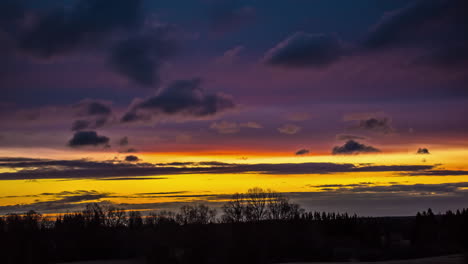 colorful sunrise lights the sky at dawn above the forest trees in silhouette - time lapse