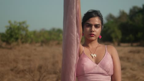 mujer con vestido rosa sosteniendo tela transparente con expresión serena, al aire libre durante el día, luz natural