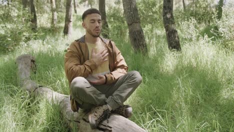 African-american-man-sitting-on-tree-trunk-and-meditating-in-forest,-slow-motion