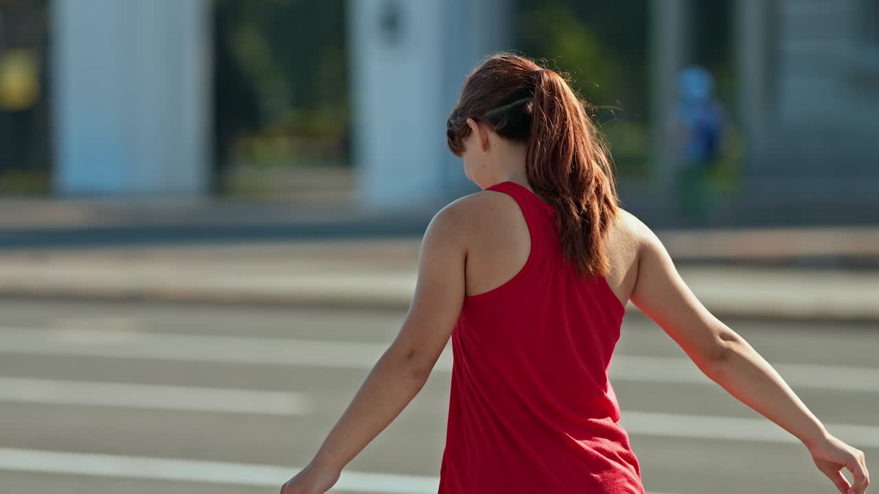 Young woman rides on roller skates, balances with her hands. Woman moves her body, turns her shoulders. View from the back. 4k, 10bit, ProRes