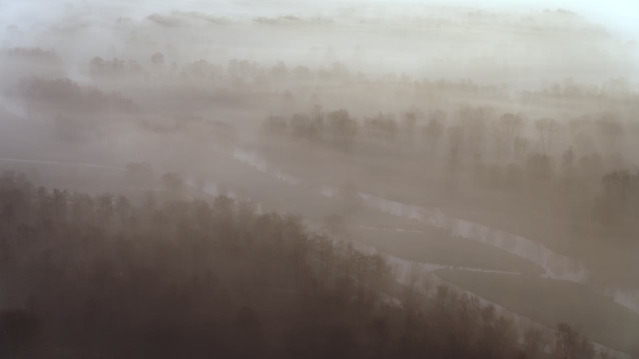 Slow aerial dolly shot over a fog shrouded river with forest and hills feels cold, gray and mysterious