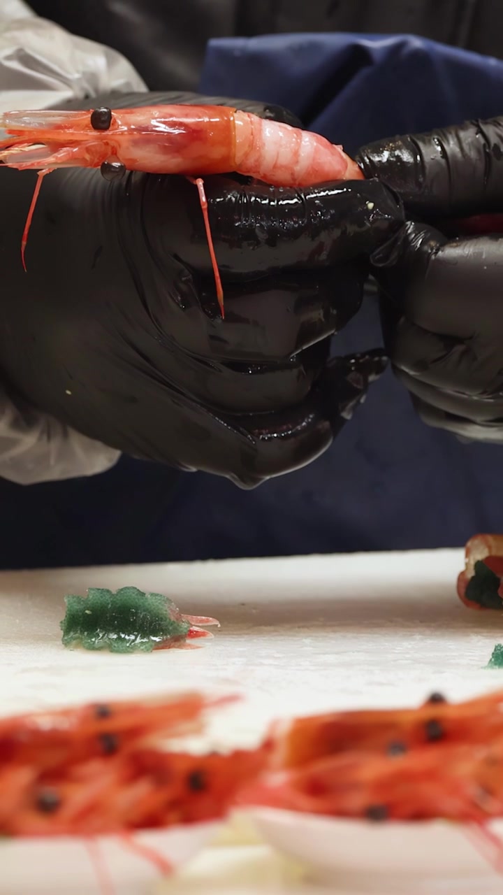 Close-up of chef in black gloves peeling raw prawns for sushi in Tokyo, Japan.