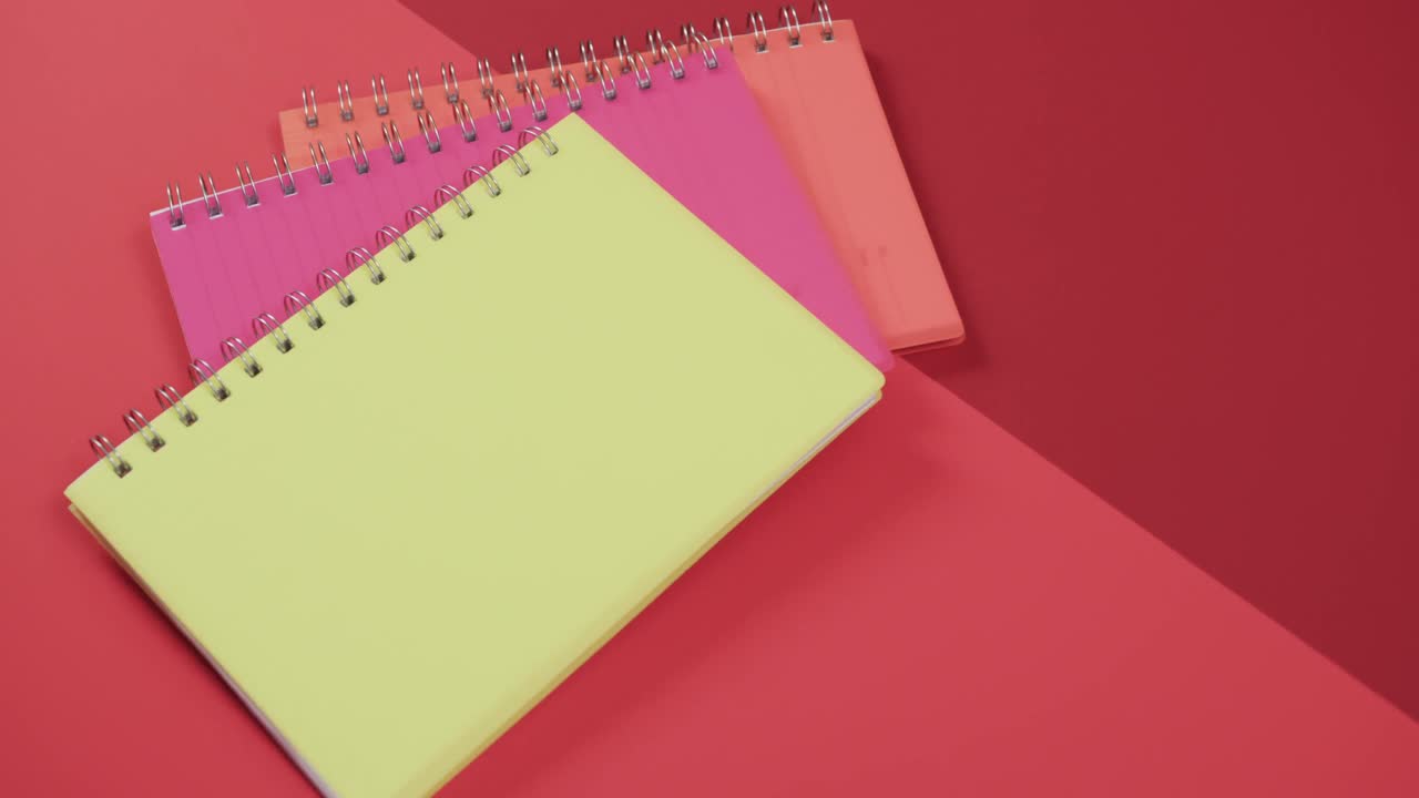 vista aérea de cuadernos coloridos sobre fondo rojo, en cámara lenta