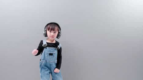 Child-listening-to-music-with-headset-wearing-jeans-on-gray-background-in-studio