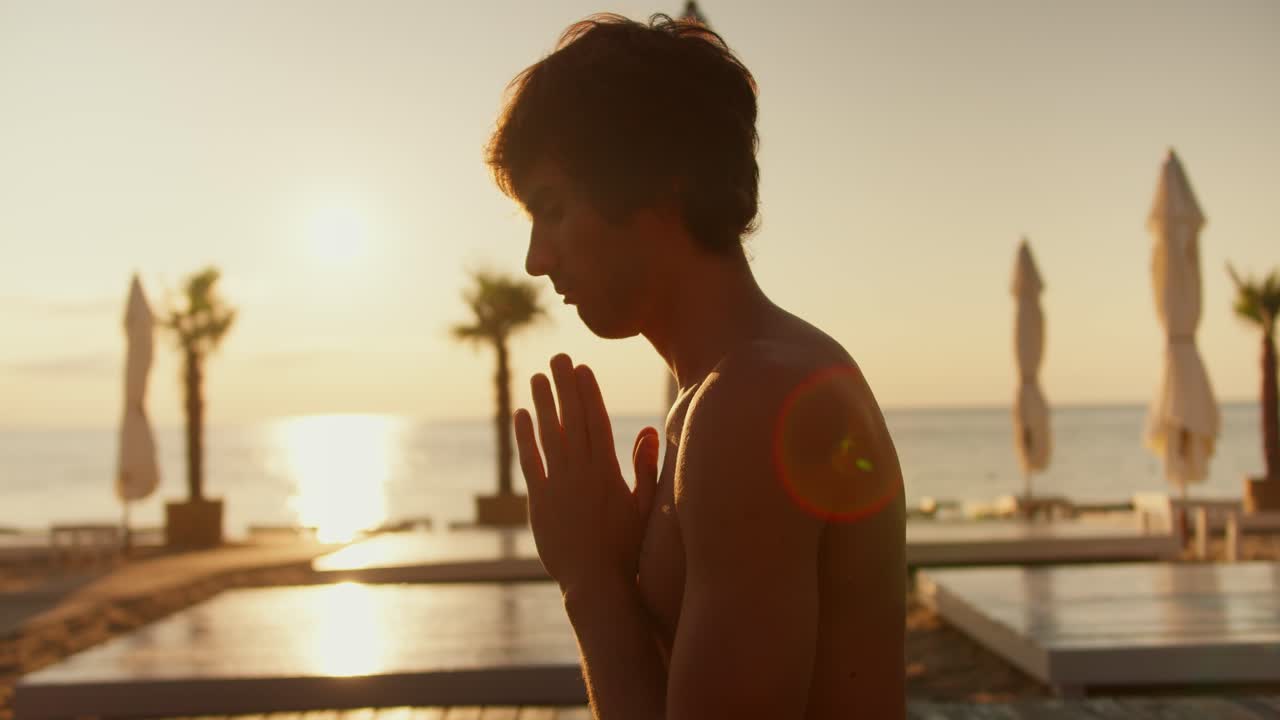 Close-up shot of a guy meditating on a sunny beach in the morning