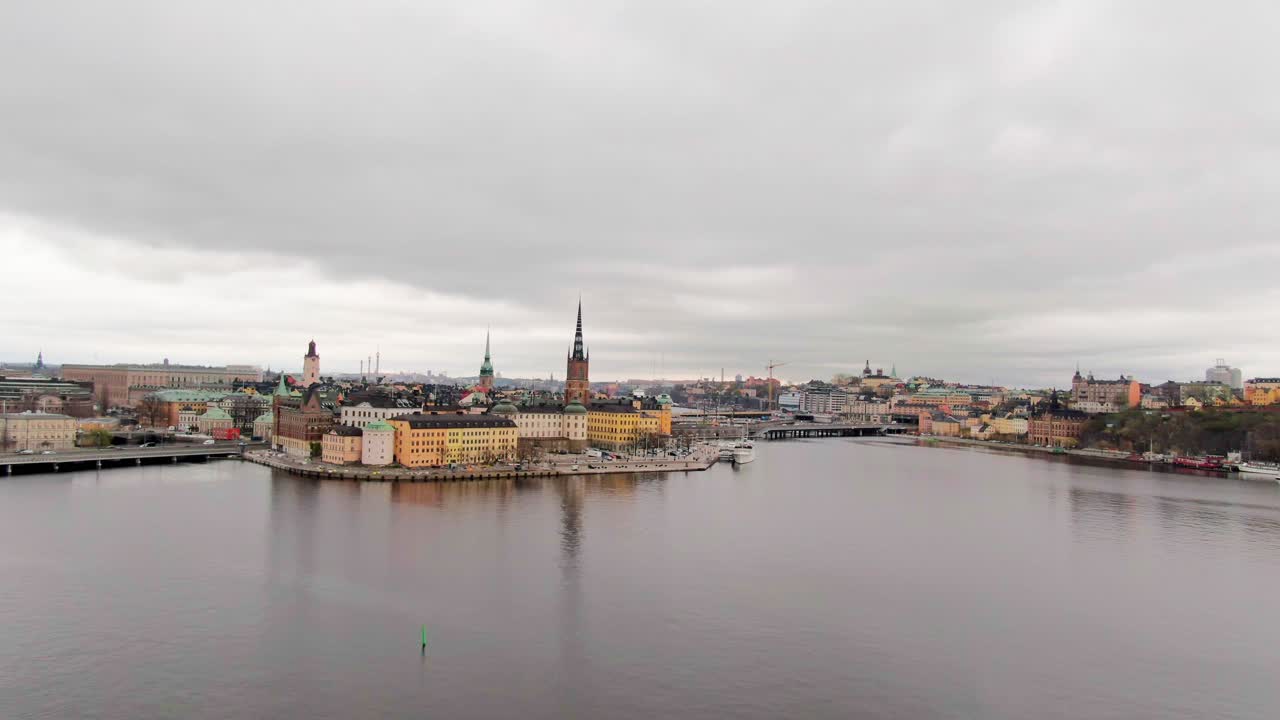 Very wide aerial approaching central Stockholm, early spring day with very cloudy skies, revealing horizon and vast waters