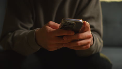 primer plano de un hombre que pasa la noche en casa sentado en el sofá con auriculares inalámbricos transmitiendo música o viendo contenido desde el teléfono móvil 1