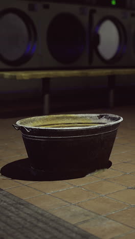 empty bucket in a dimly lit laundromat during late night hours