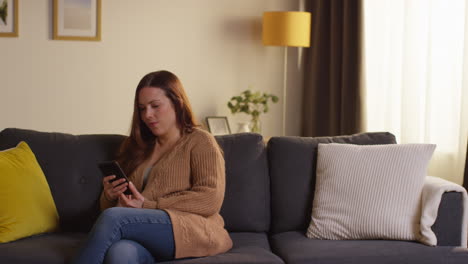 Mujer-Sentada-En-Un-Sofá-En-Casa-Viendo-Una-Película-O-Programa-O-Navegando-Por-Internet-En-Un-Teléfono-Móvil-2