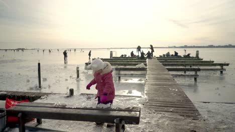 cute little girl playing with ice crystals, children riding a sledge and ice skating in durgerdam village frozen pond on a sunny winter day