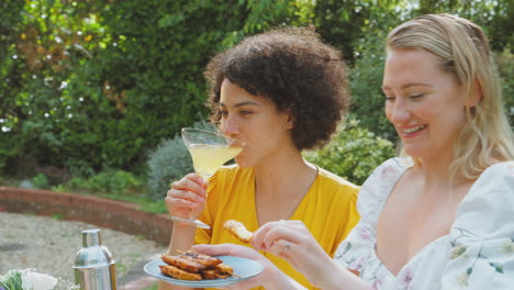 Tres-Amigas-Sentadas-Al-Aire-Libre-En-El-Jardín-De-Verano-En-Casa-Bebiendo-Cócteles-Y-Comiendo