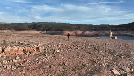 hombre irreconocible caminando hacia el pantano seco en el embalse de sau, españa