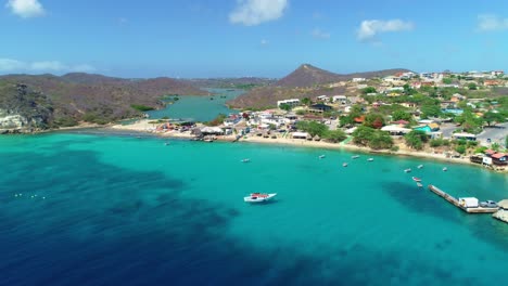 drone dolly above deep blue turquoise ocean water, hills, salt pan, and homes near coast