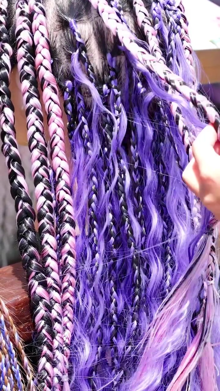 Manos trenzan extensiones de cabello coloridas en un animado entorno callejero de Phuket, mostrando patrones intrincados y tonos vibrantes.