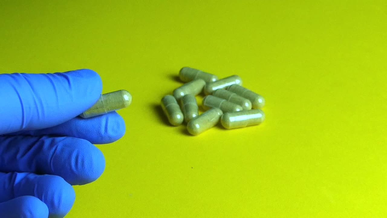 Gloved hand holding a natural herbal supplement capsule over a yellow laboratory background