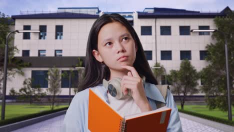 close up of asian teen girl student with a backpack reading book and thinking and looking around while standing in front of a school building