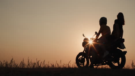 silhouettes of a romantic couple sit on a motorcycle at sunset