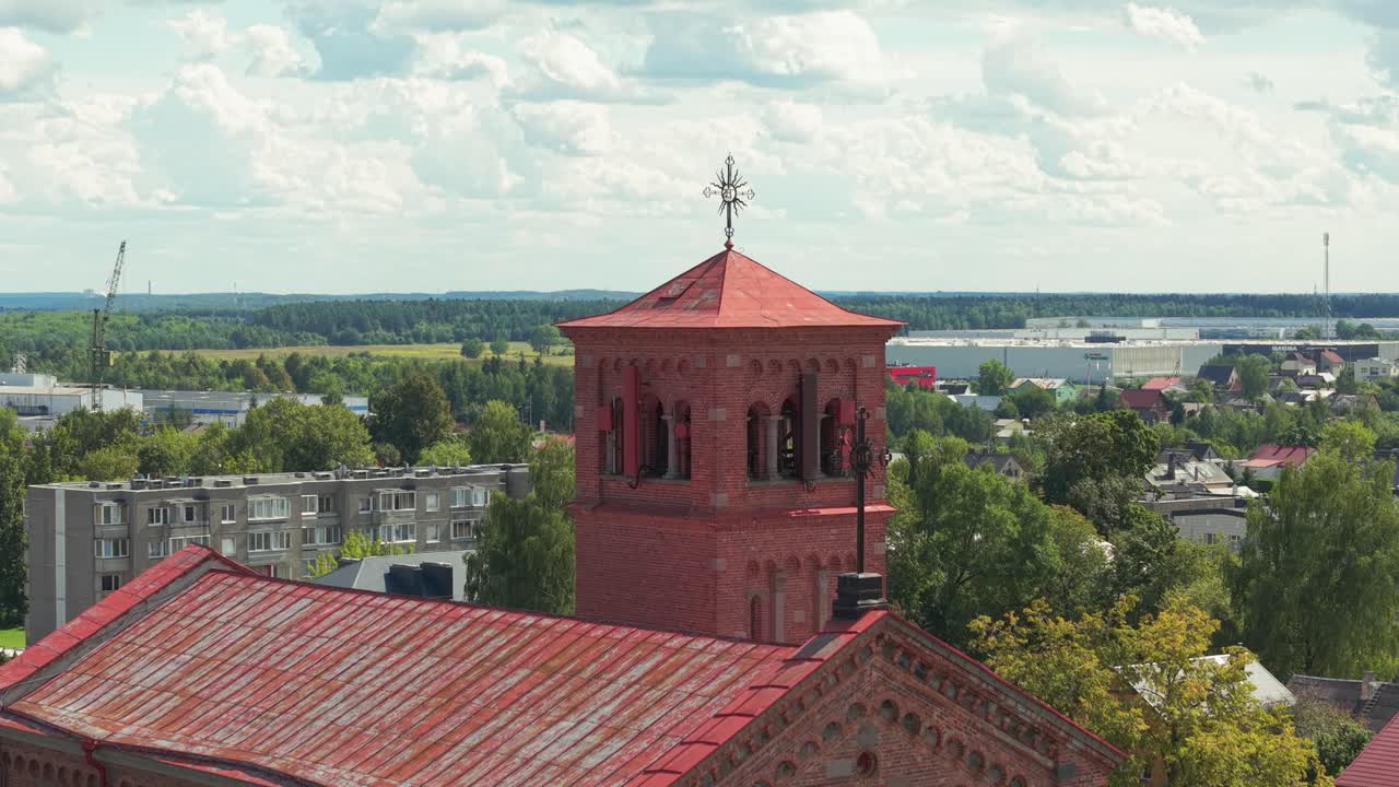 Close-up aerial view of the red brick tower of Lentvaris Church in Lithuania, with scenic townscape and lush green surroundings under a bright summer sky