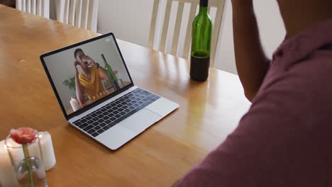 Mid-section-of-african-american-man-drinking-wine-while-having-a-video-call-on-laptop-at-home