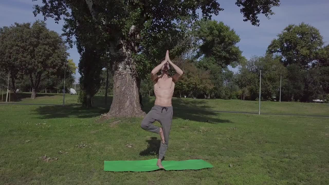 Jovem atlético e esguio une as mãos em postura Namastê, homem atlético pratica yoga ao ar livre.