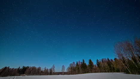 View-of-white-snow-covered-field-with-forest-in-the-background-from-evening-to-night-in-timelapse