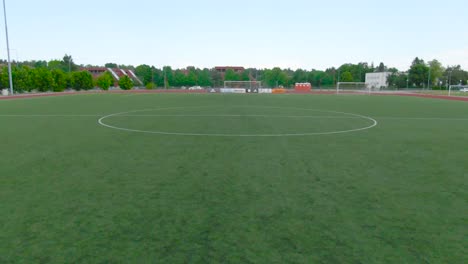 aerial drone footage fly over from saue laagri soccer or football stadium during cloudy weather summer or autumn time. green trees, asphalt roads, cars and houses in the background. cars driving too.