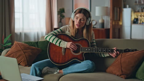 headphones woman guitarist composing music at acoustic guitar at home couch.