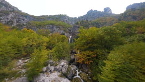 flight up a mountain river to a waterfall through autumn coloured forest in theth, albania