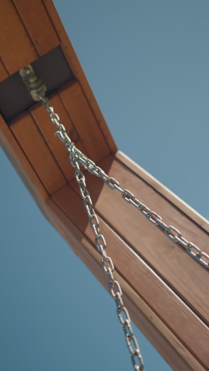 primer plano de columpio y cadena de madera moviéndose suavemente bajo un cielo azul claro y brillante, destacando la simplicidad, la relajación al aire libre y la artesanía en un entorno natural pacífico