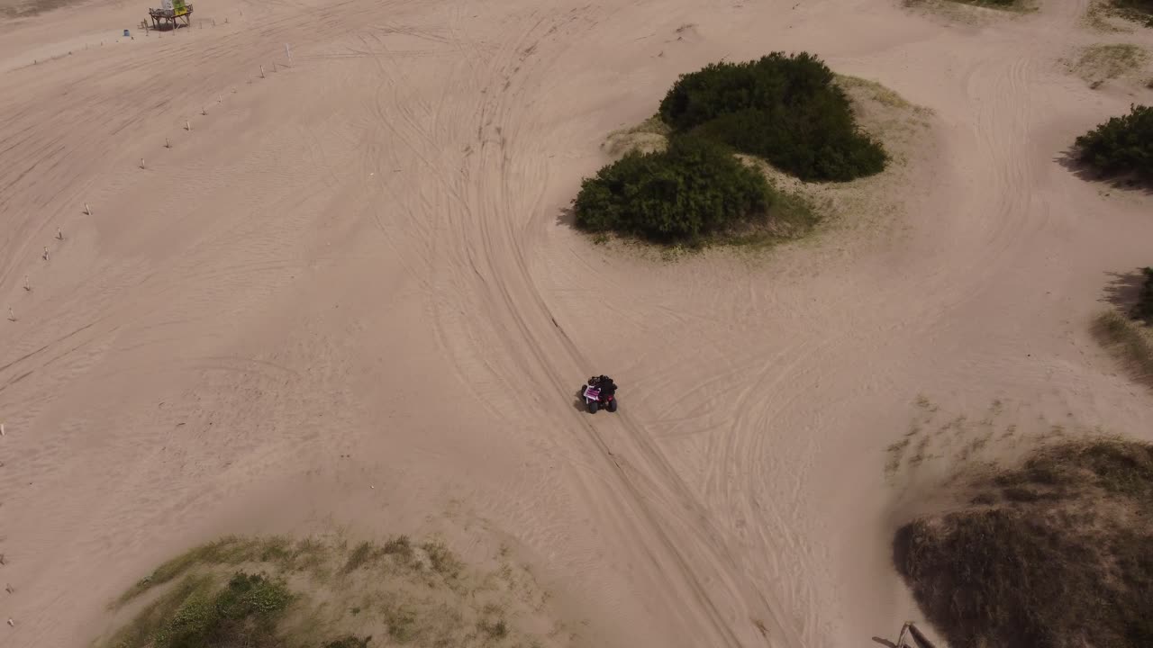 Aerial moving view of a person driving a quad bike on the beach sand in a forest background in Mar de las Pampas, South America