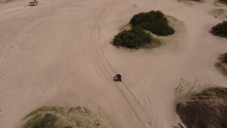 aerial moving view of a person driving a quad bike on the beach sand in a forest background in mar de las pampas, south america