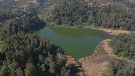 Low-drone-flight-over-Dieng's-Telaga-Warna,-the-color-changing-lake-and-forests-in-Java,-Indonesia