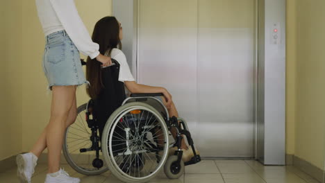 woman and disabled friend in wheelchair stand near elevator