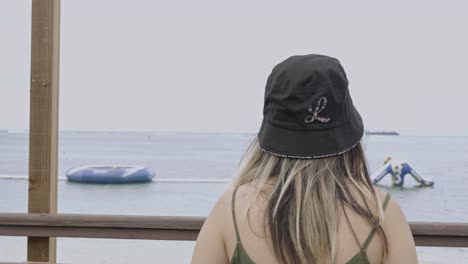 Back-view-of-girl-walking-towards-the-wooden-railing-to-look-at-the-beach,-slow-motion