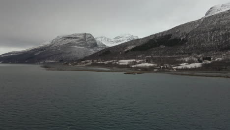 Drone-shot-flying-over-a-fjord-with-snow-capped-mountains-in-Balsfjord,-Norway