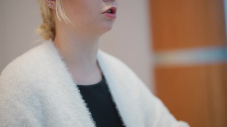 Three-quarter side profile shows person in fluffy white cardigan layered over black ribbed top, with subtle hand motion near hem, soft posture shift, and warm indoor light creating cozy fashion detail