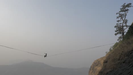 a young indian boy trying to balance and walk in a sling high above the valley surrounded by pinnacles