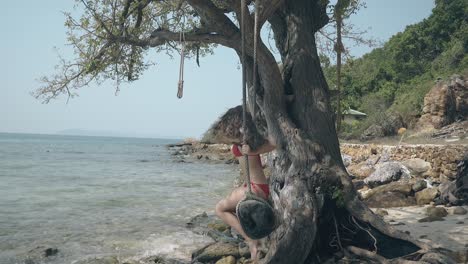 young lady with loose hair swings on log at sea shore