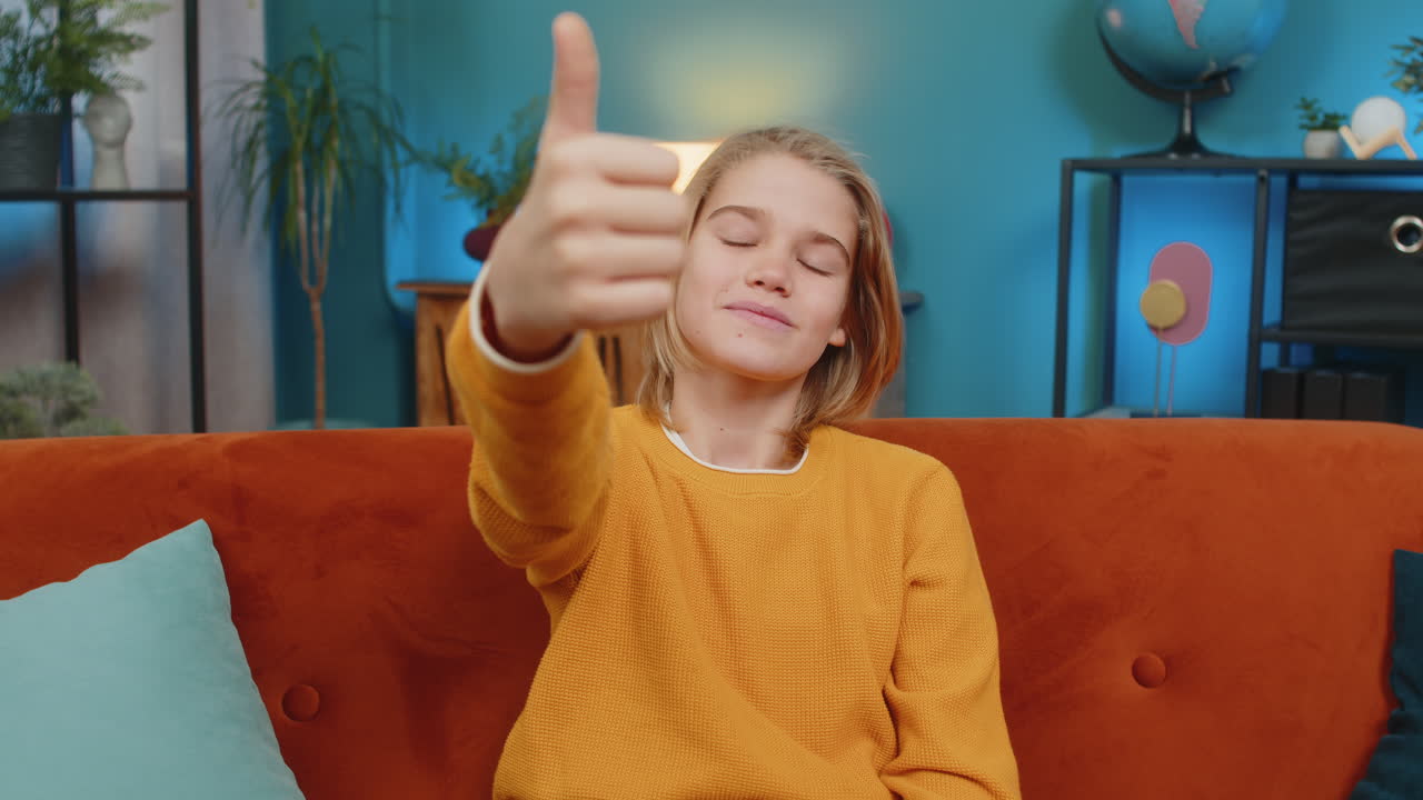Teenager smiling boy giving thumbs up like to camera satisfied with result sitting on sofa at home