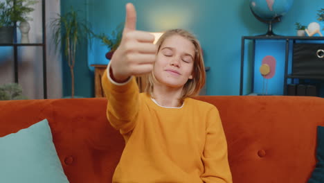 teenager smiling boy giving thumbs up like to camera satisfied with result sitting on sofa at home