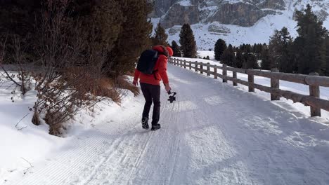 videógrafo caminando con chaqueta de nieve roja usando cámara profesional montada en gimbal estabilizador dji rs 3 mini rodeado de paisaje montañoso nevado