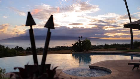 static shot of pool deck view of sunset behind lanai with hot tub and torches on in maui hawaii