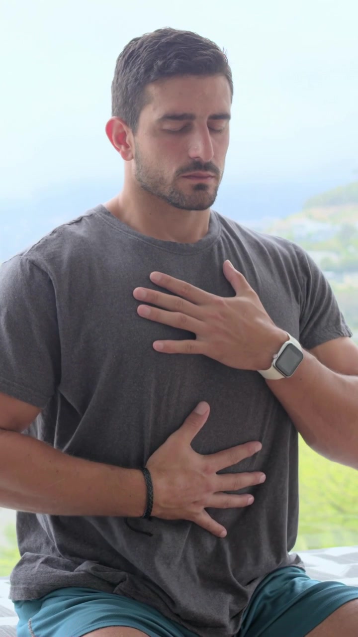 Placing hands on chest and abdomen, adult man breathing on balcony overlooking hillside, centering