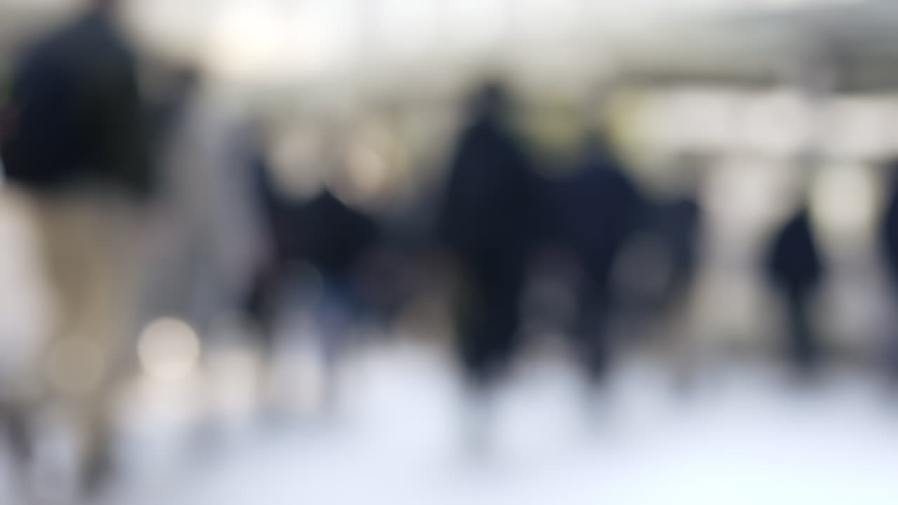 Silhouette sfocata di una folla che cammina attraverso una piazza urbana illuminata dal sole.