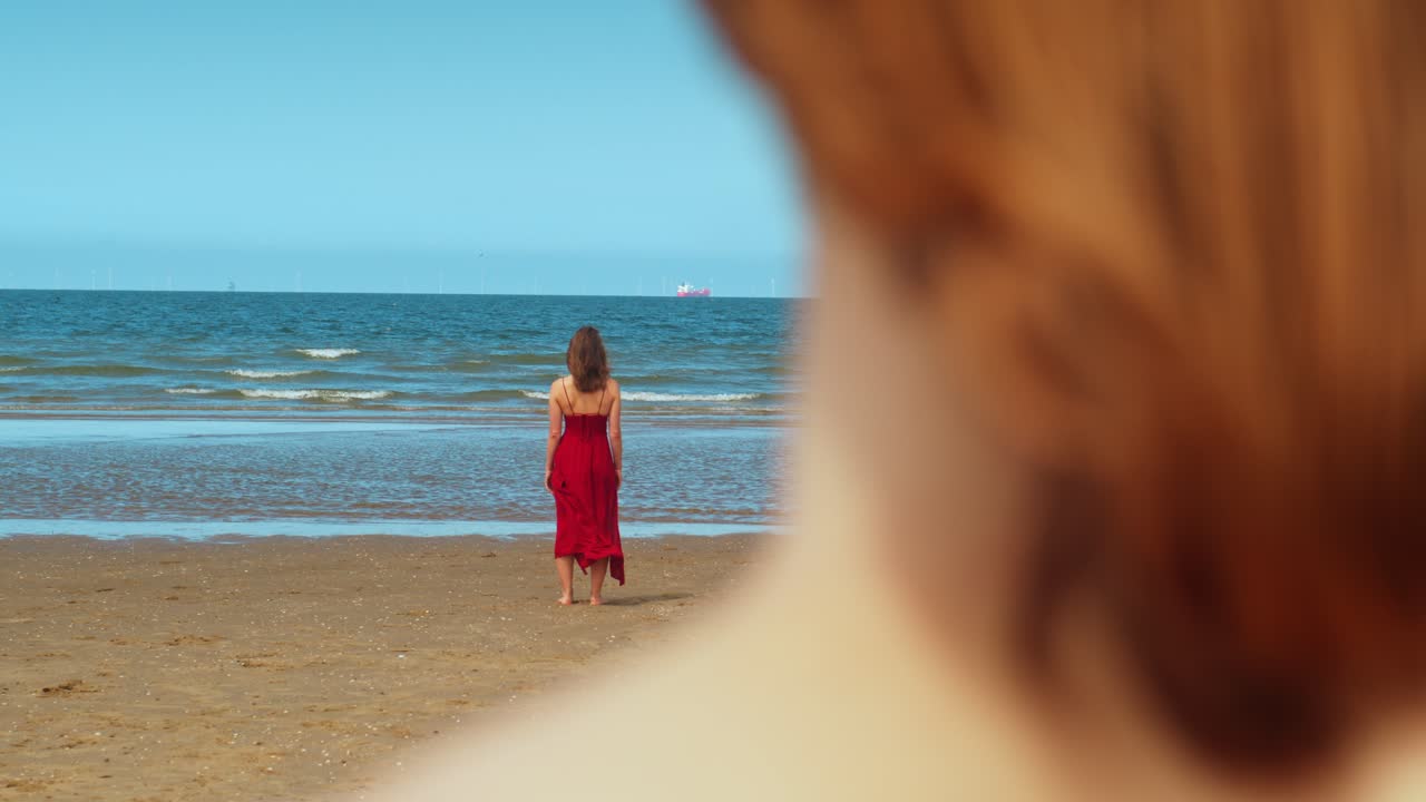 A Man Gazes at a Woman in a Red Dress Standing on the Beach in Scheveningen, Netherlands - Defocused Shot