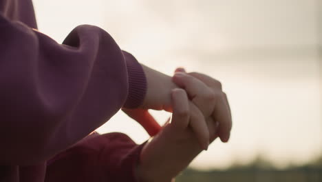 close-up of woman hand in maroon clothing performing wrist twist with fingers locked together, sunlight creating a glowing effect around her hand