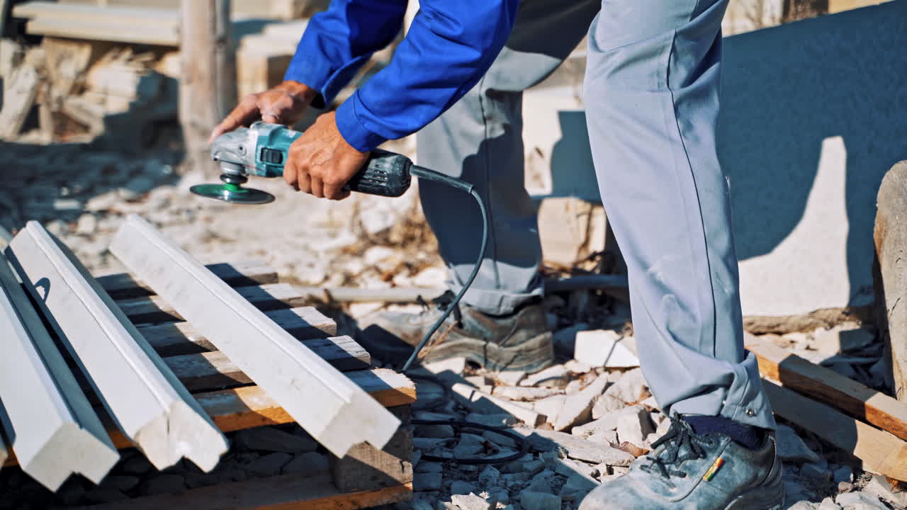 Laborer polishes stone with hand grinder outdoors. Man worker is polishing stones by hand grinding machine on the open air.