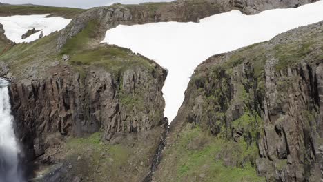 Jagged-cliffs-in-Iceland-with-meltwater-from-snow-flowing-through-canyon,-aerial